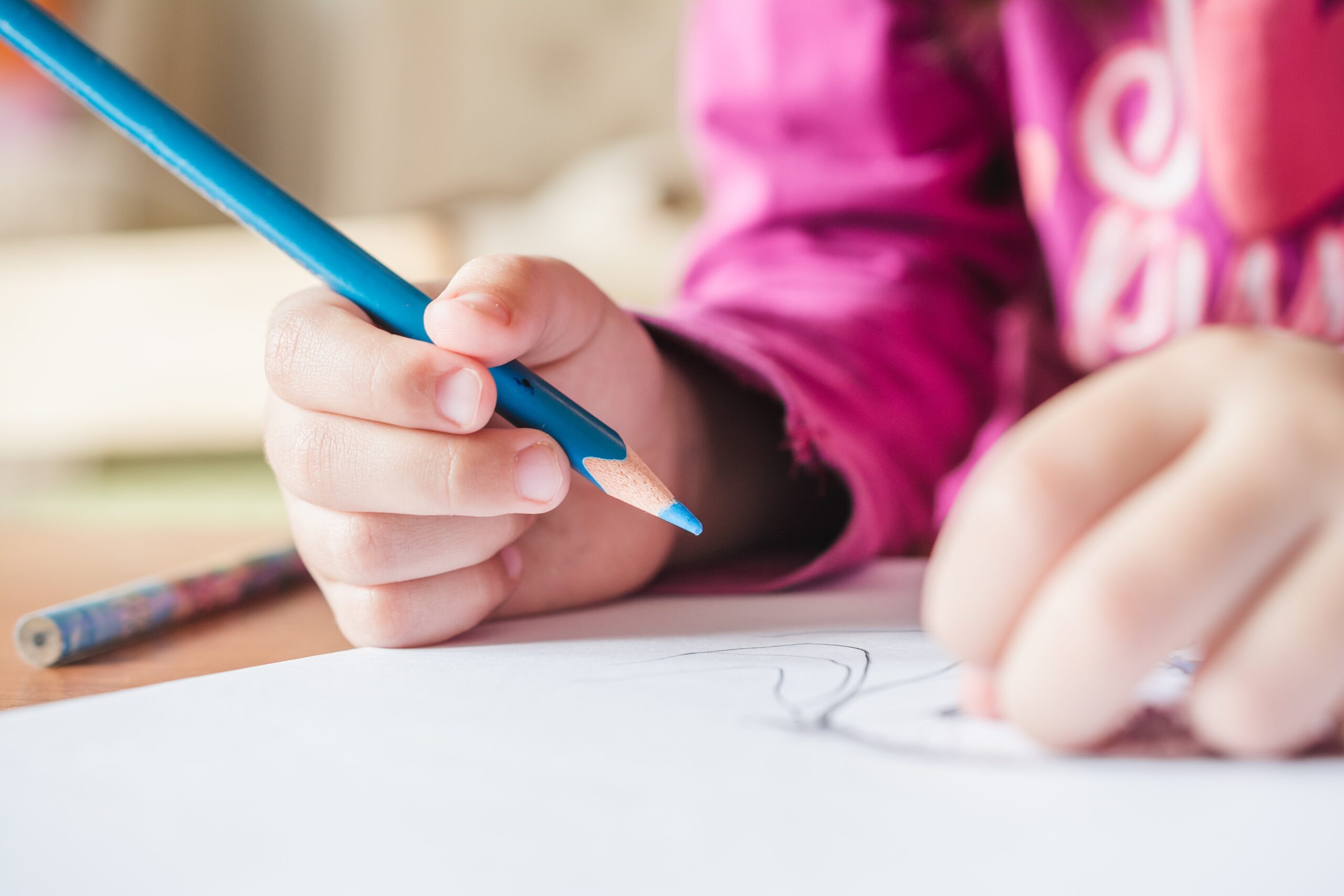 shallow focus shot of a child wearing a pink t shirt painting a picture with the blue colored pencil